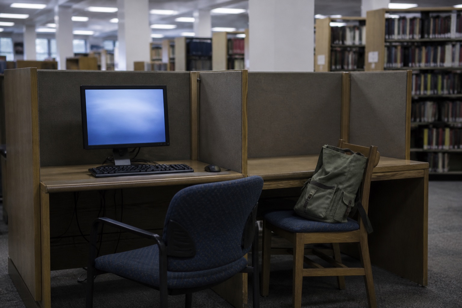 An empty library computer carrel, chair pushed back, as if the last person just left