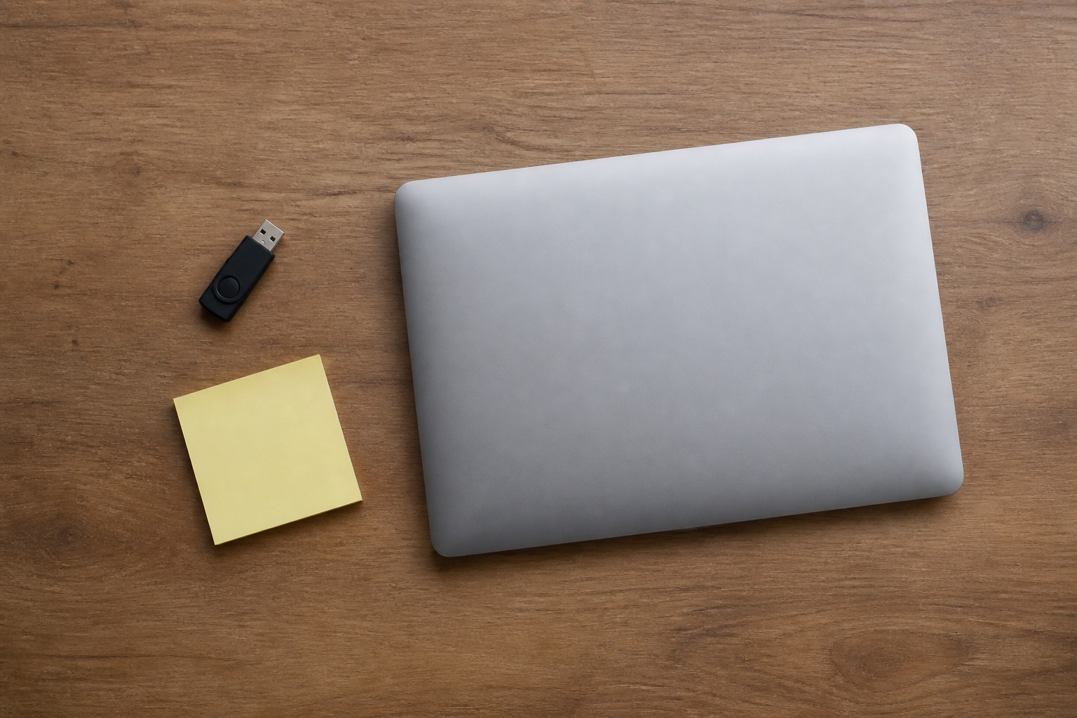 A USB stick, a blank sticky note, and a closed laptop on a wooden desk